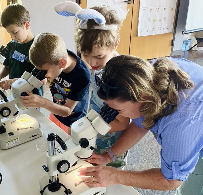 教育工作者用显微镜观察孩子, 另外两个孩子在背景中使用显微镜